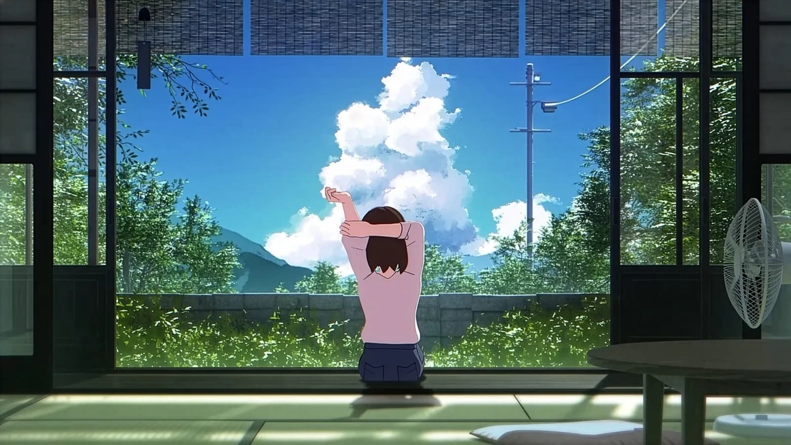 A person stretches with their back to the viewer, looking out a large window at a lush green landscape under a bright blue sky with fluffy white clouds.