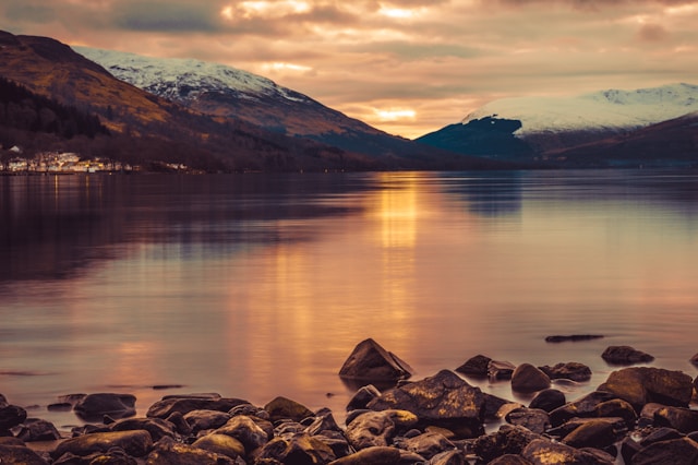 Dusk over Loch Lomond, with soft light reflecting off the calm waters, surrounded by gently sloping hills.