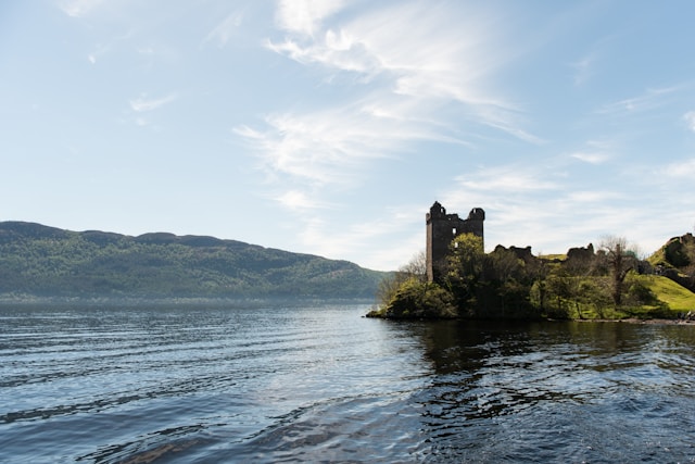 Urquhart Castle overlooking the expansive waters of Loch Ness in Scotland, under a cloudy sky.